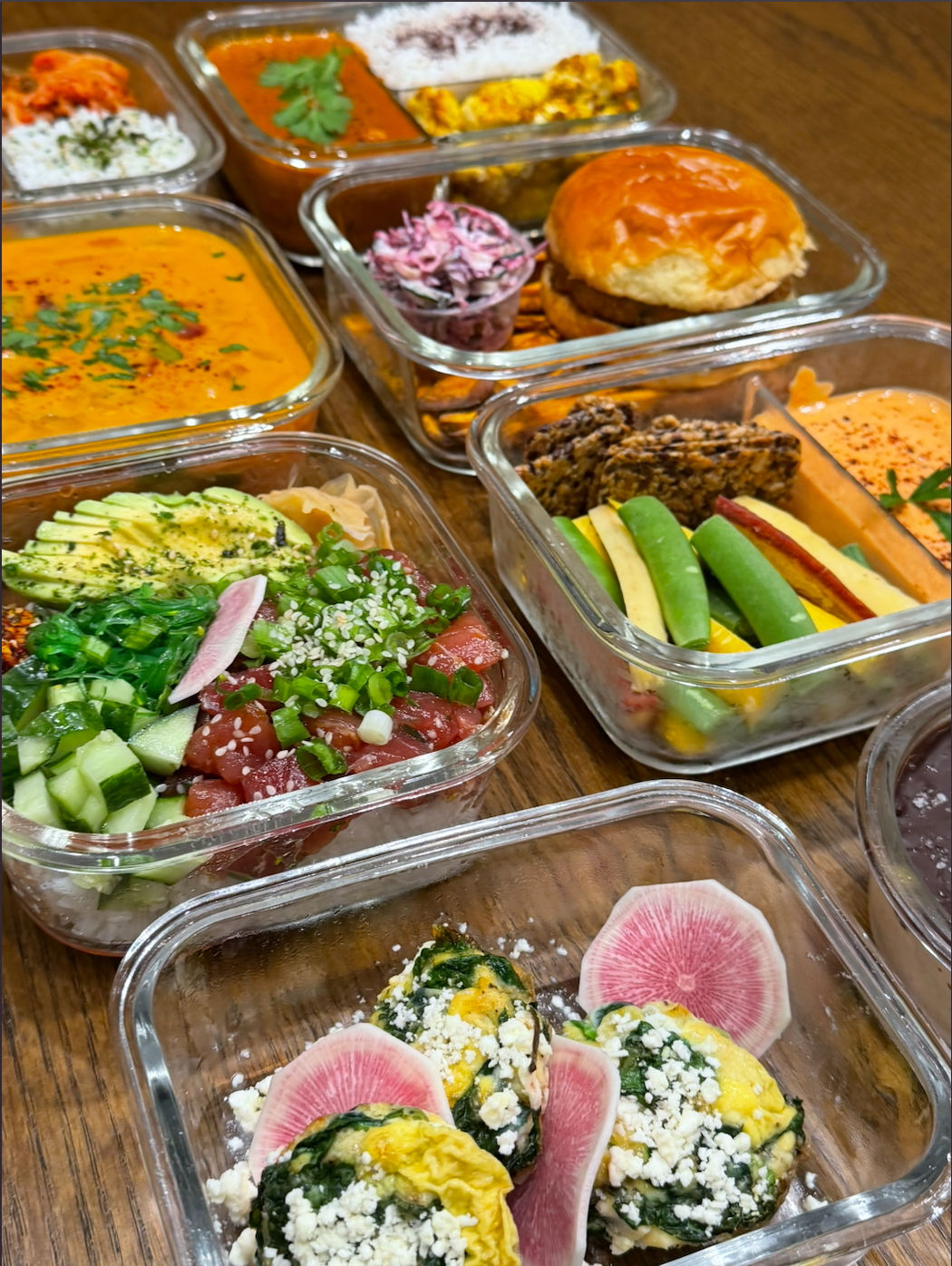 Glass containers of weekly meal prep — tuna poke bowl, spinach frittata with feta, curry with rice, sliders with slaw, soup, and crisp vegetables